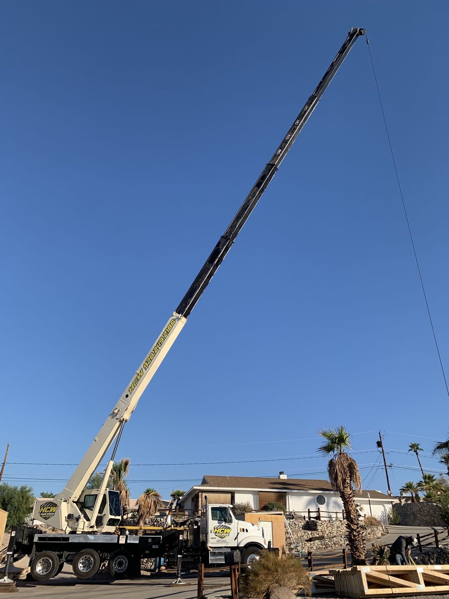 Boom truck crane on outriggers with its telescopic boom fully extended high over a residential street