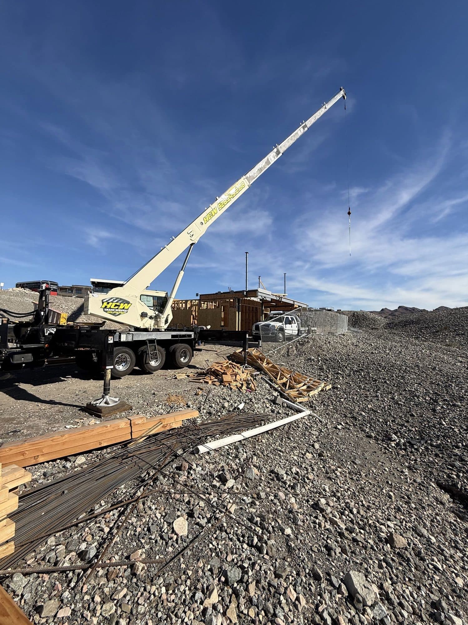 Boom truck crane on a gravel site with outrigger on a pad, wood framing and lumber nearby