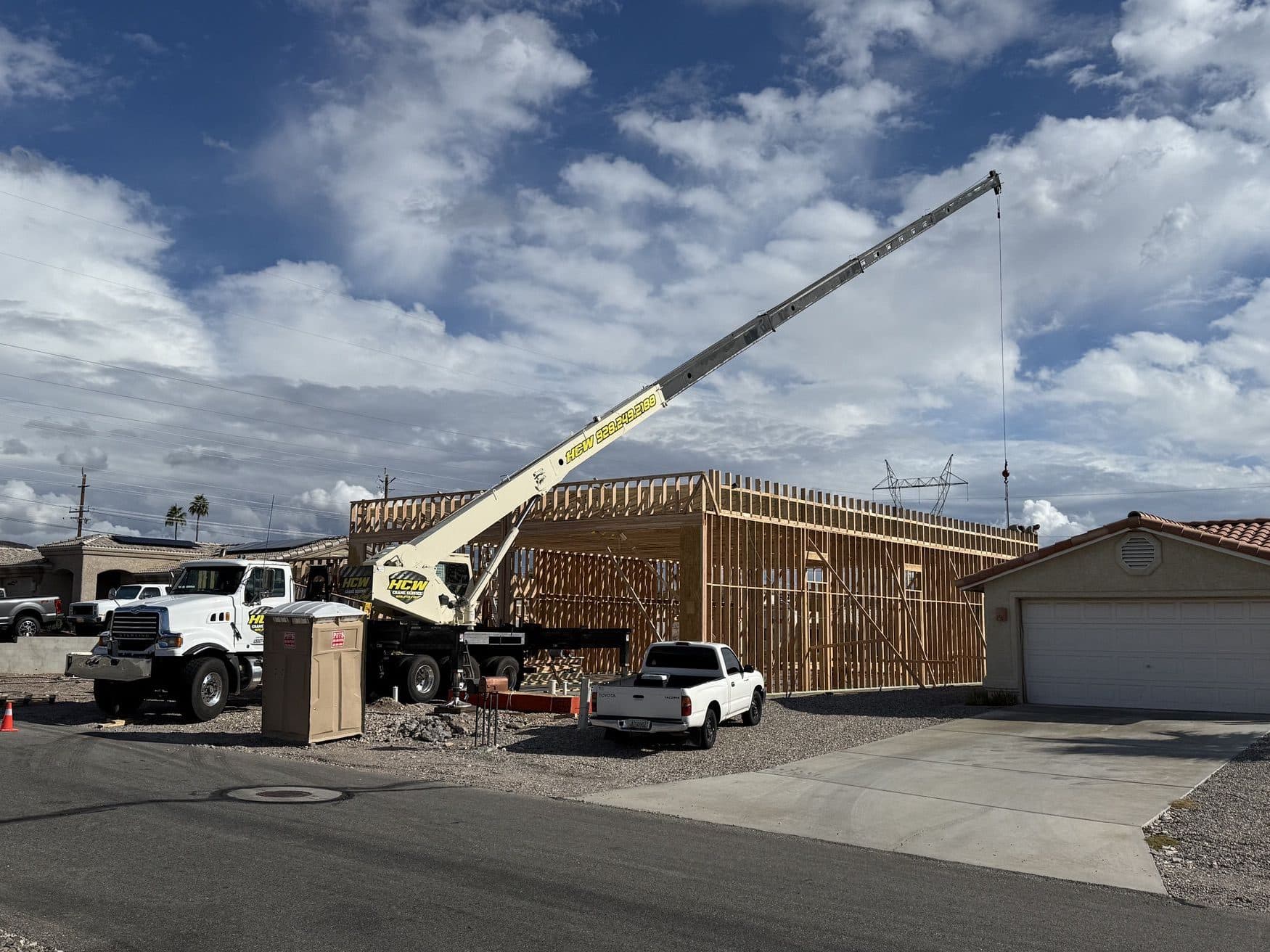 White boom truck crane with extended cream boom beside a wood framed building in a residential neighborhood