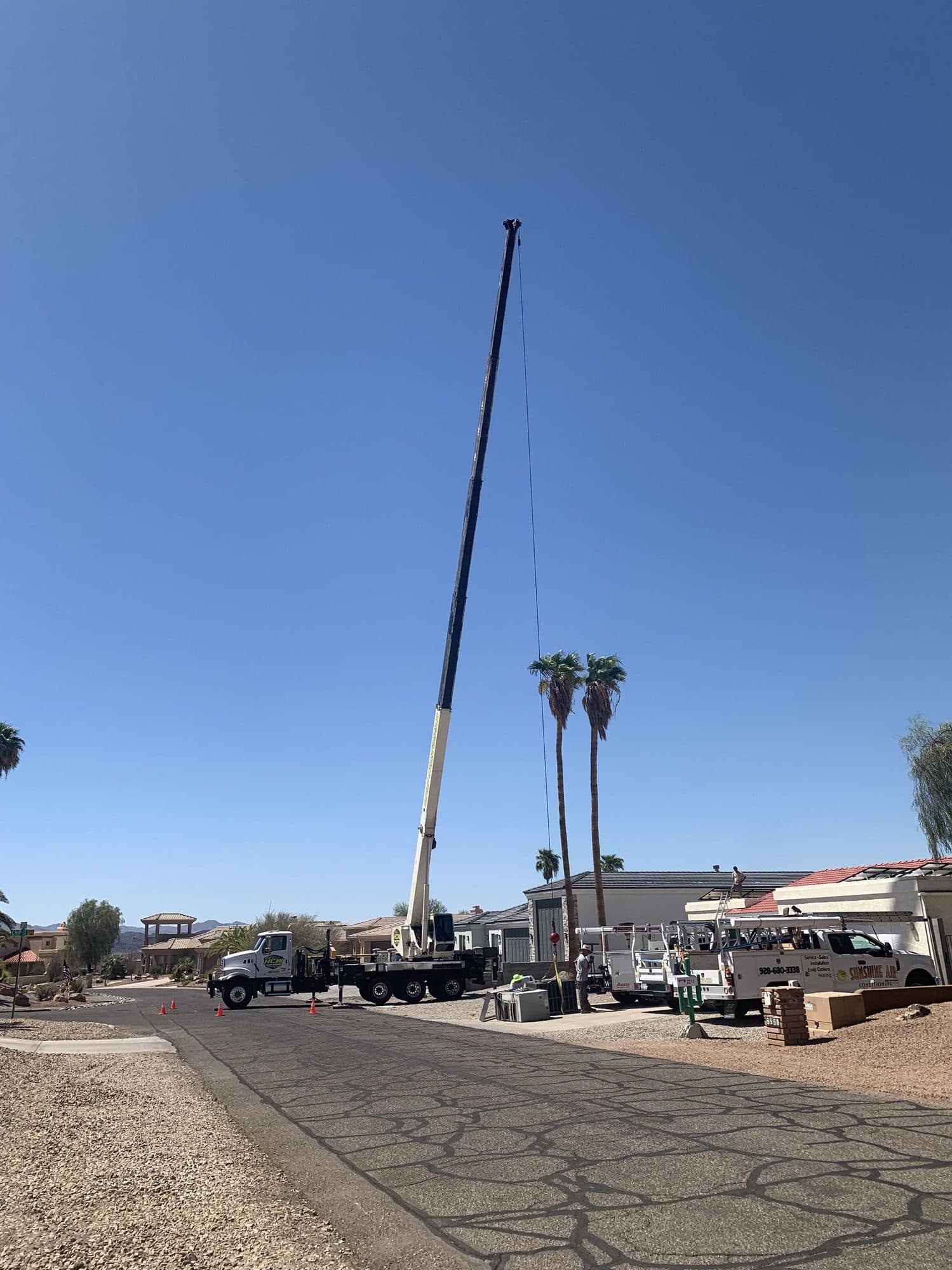 Boom truck crane with telescopic boom fully extended above a residential street during an HVAC lift