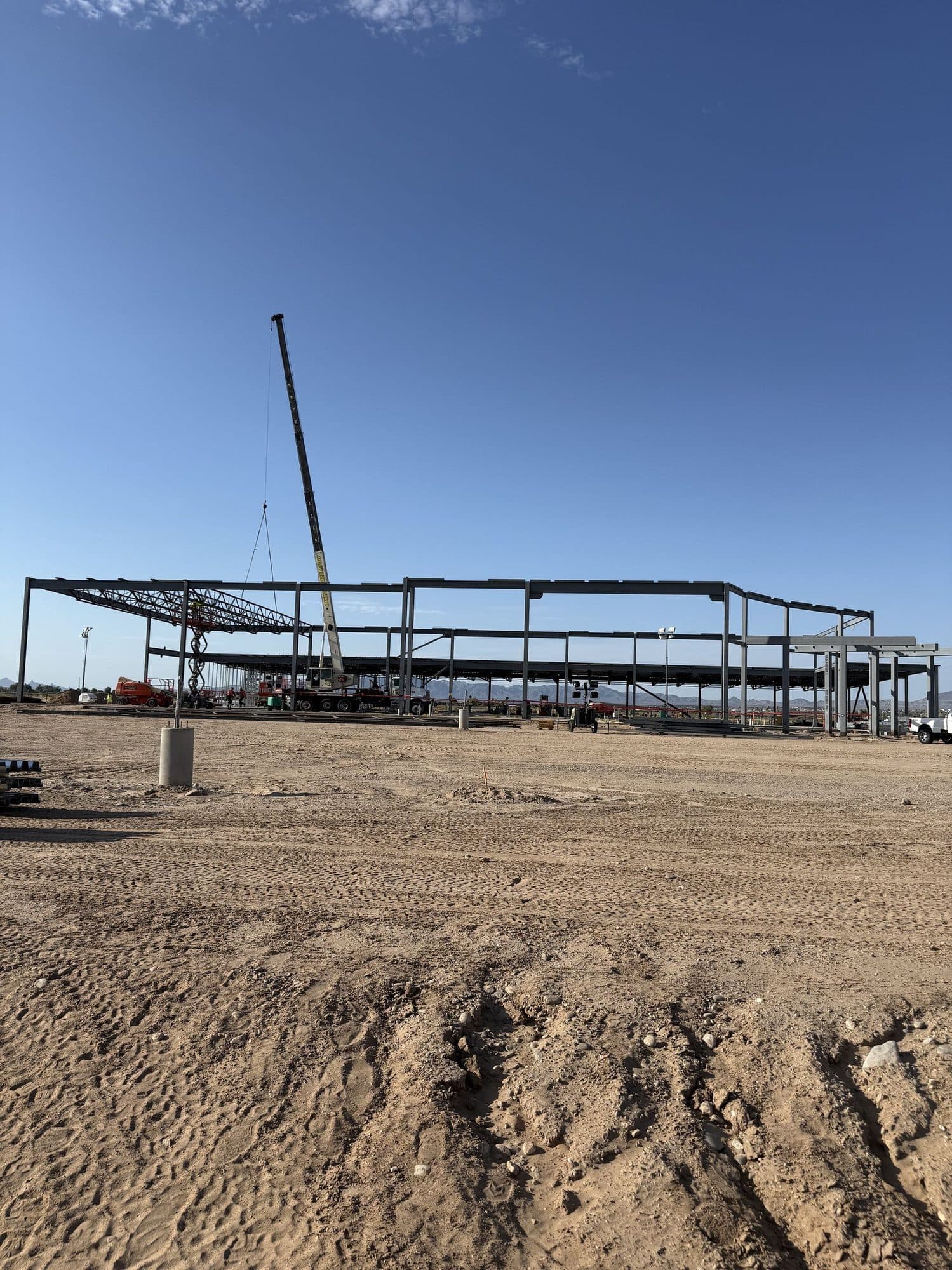 Mobile crane with boom raised inside a large steel building frame on a flat dirt site