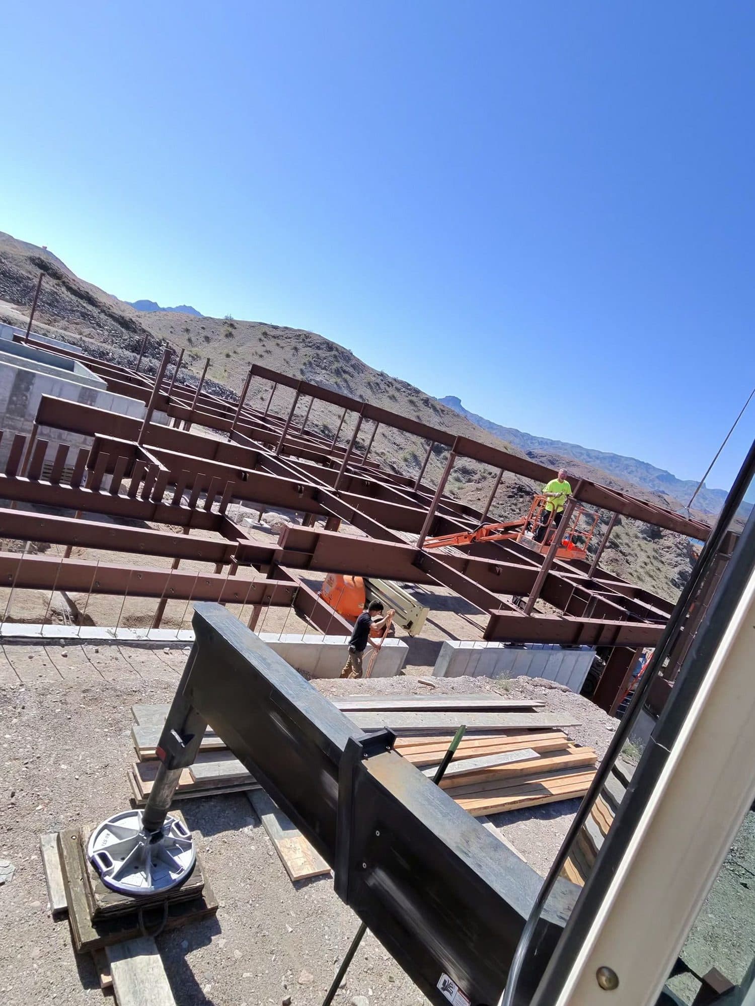 Crane outrigger resting on timber cribbing beside a rust colored steel floor frame on a desert hillside