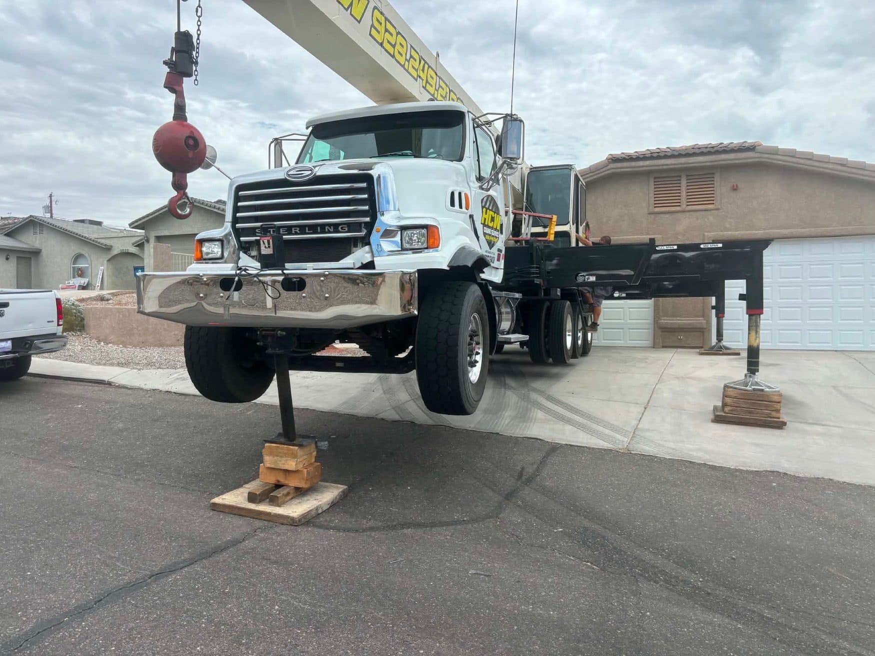 White Sterling boom truck crane leveled on outriggers with stacked wood cribbing pads in a residential driveway