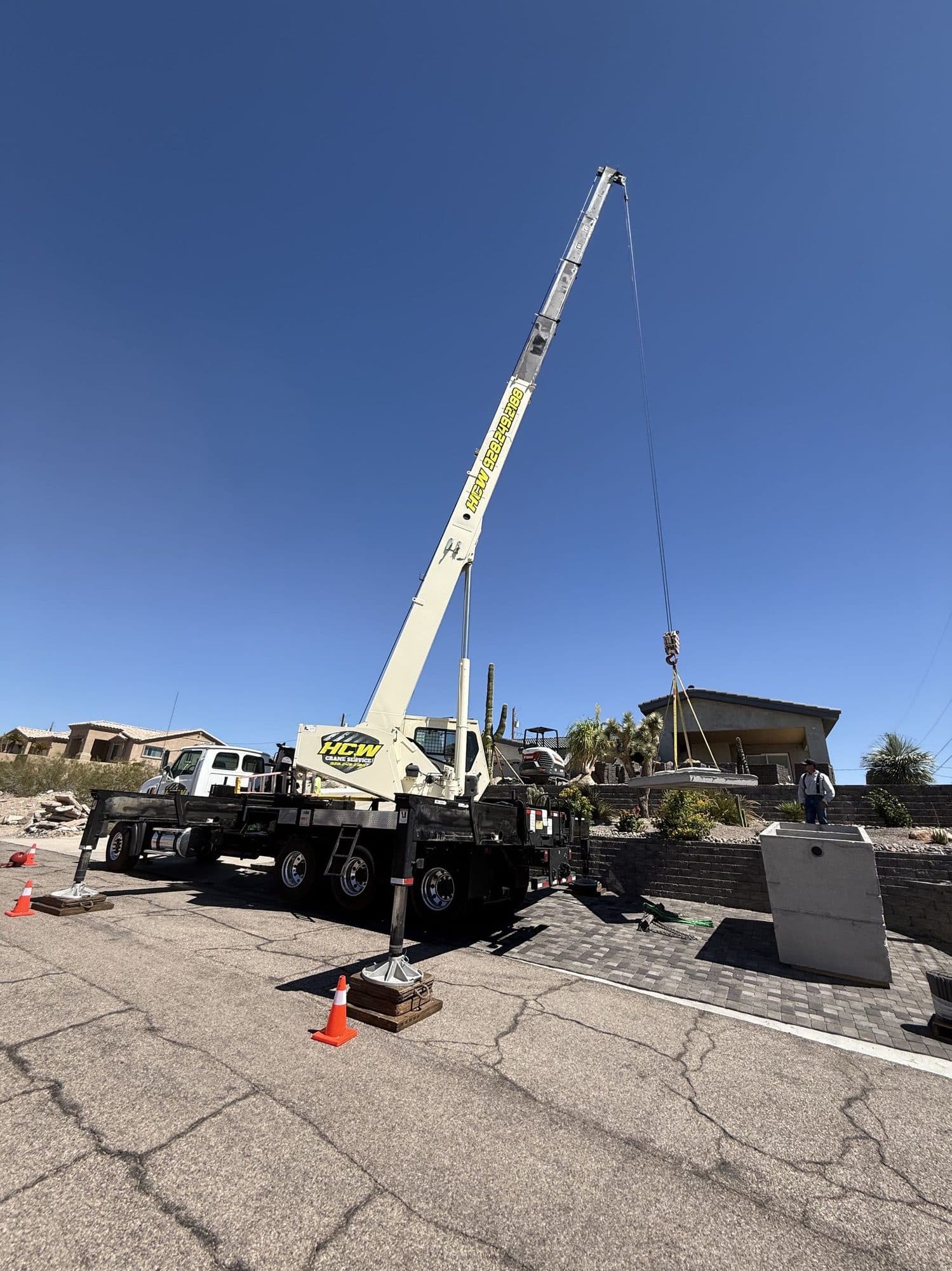 Boom truck crane on cribbed outriggers lifting a precast concrete piece into a landscaped residential yard