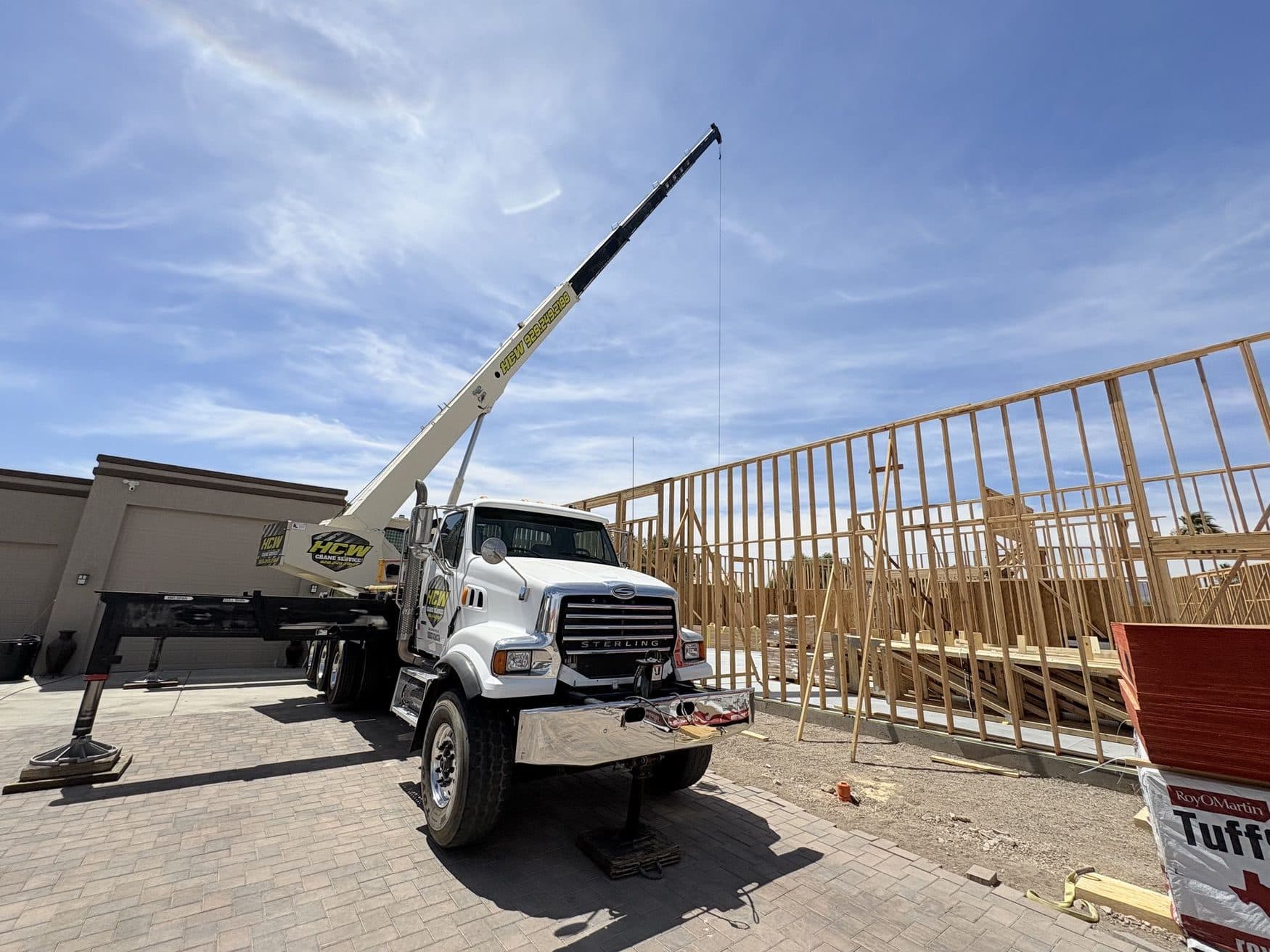 White Sterling boom truck crane on outriggers beside two story wood wall framing on a paver drive
