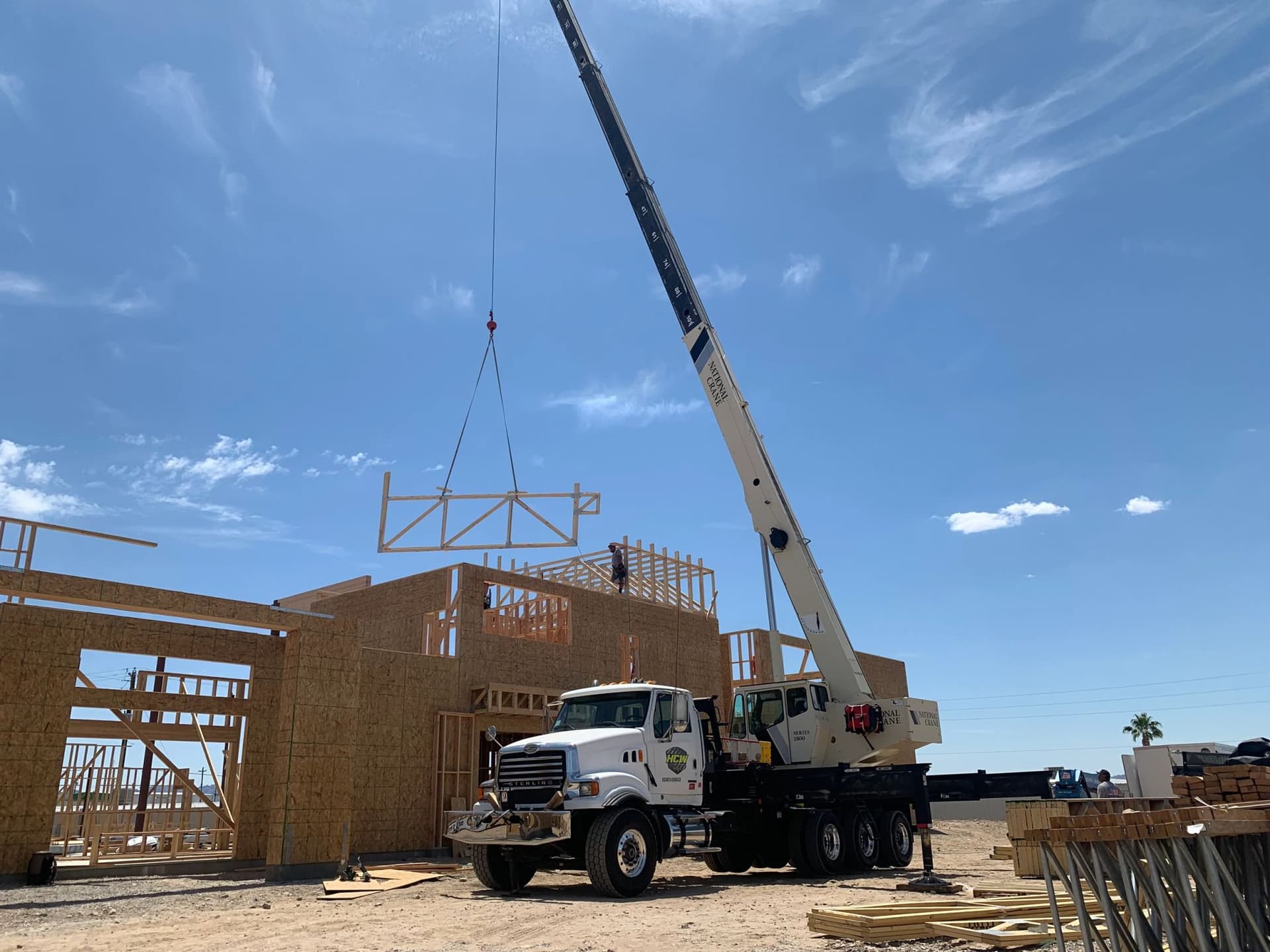 Boom truck crane setting a wood roof truss onto a two-story framed house