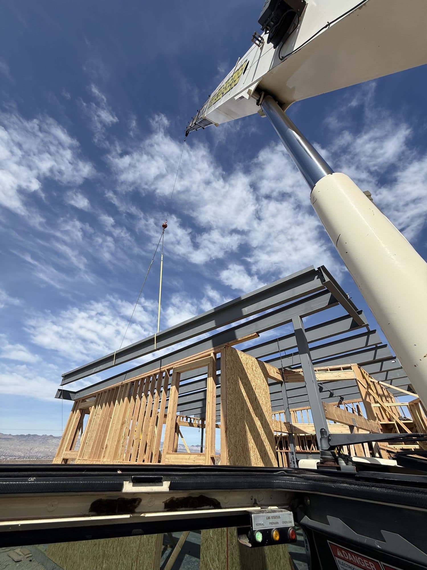 Operator view from the crane cab, boom overhead, steel beams landing on a wood framed house