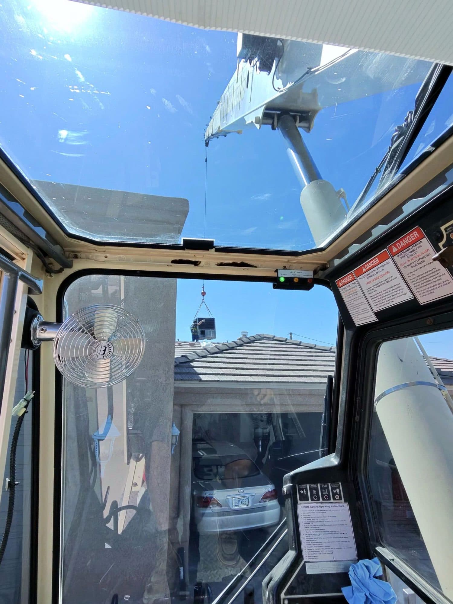 Rooftop unit hanging from the crane hook above a tile roof home, seen through the crane cab windows