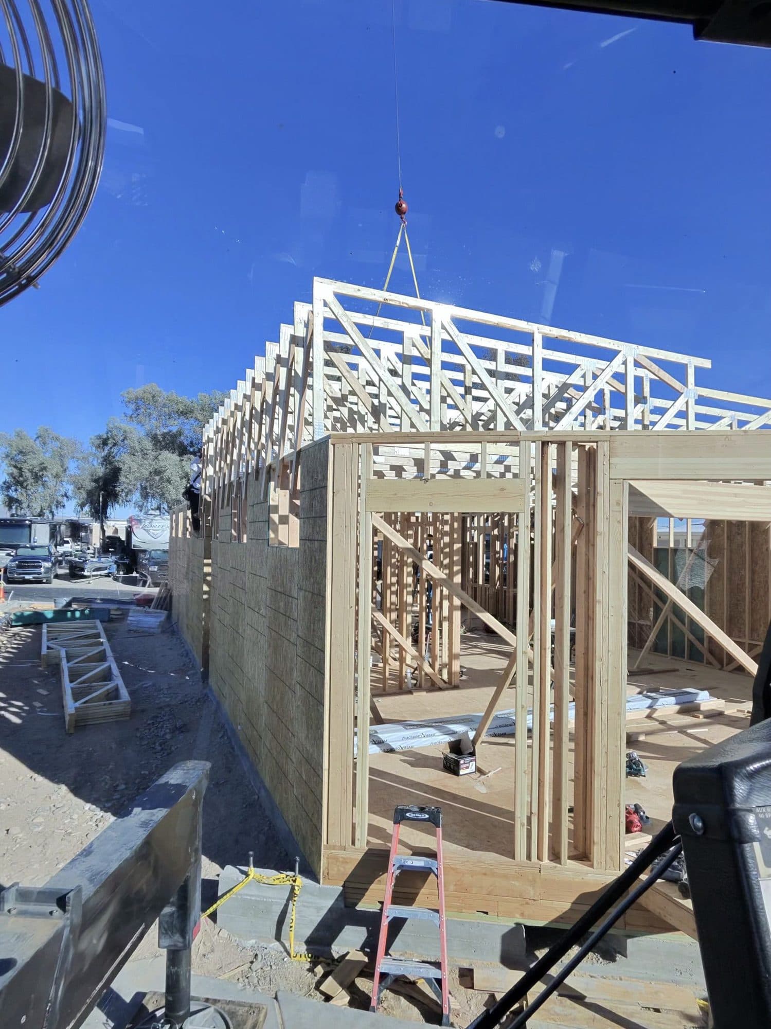 Rigged trusses set atop a new wood house frame, seen from the crane cab with the hook above