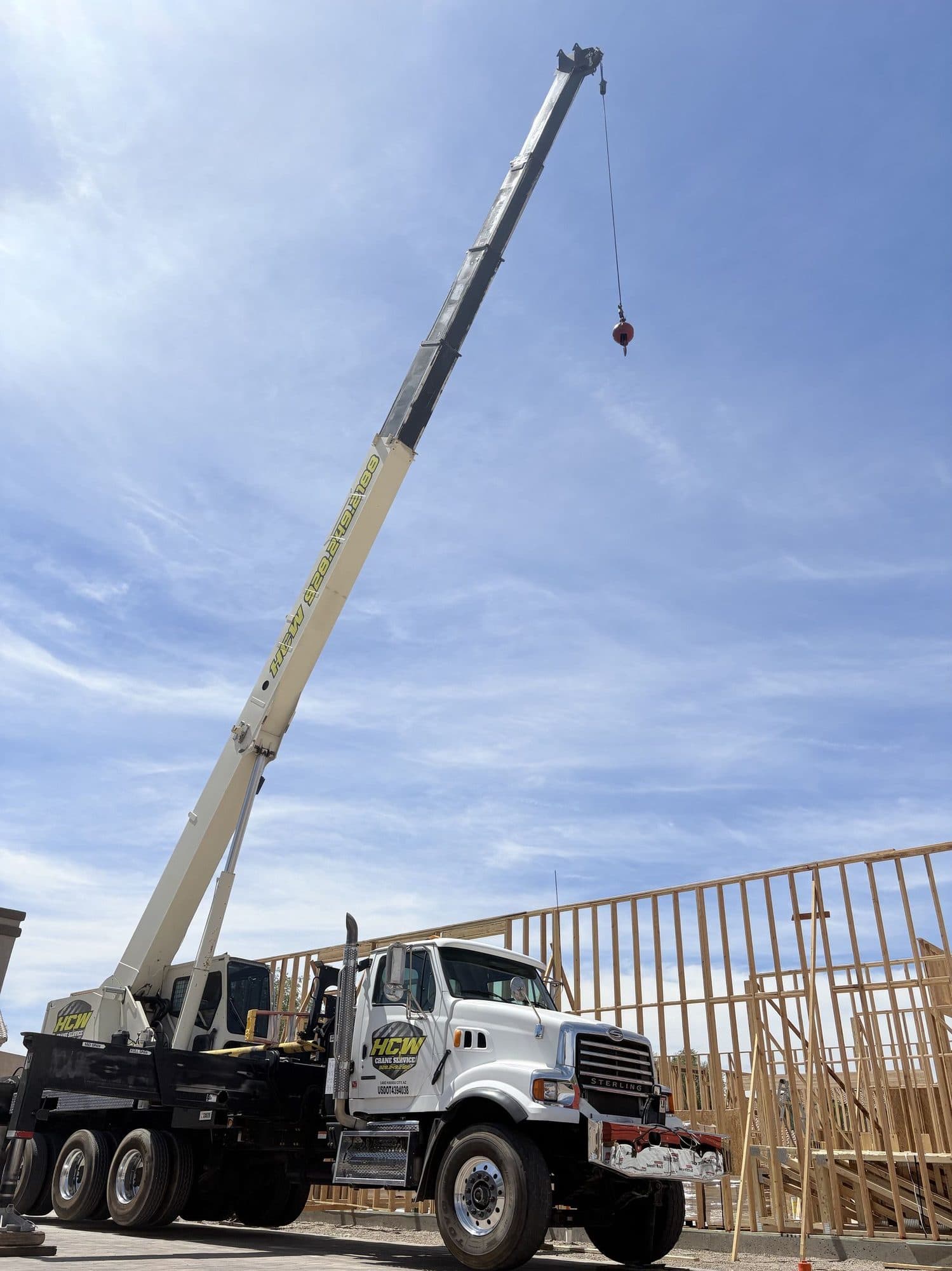 Low angle view of a white Sterling boom truck crane with boom raised beside wood framing