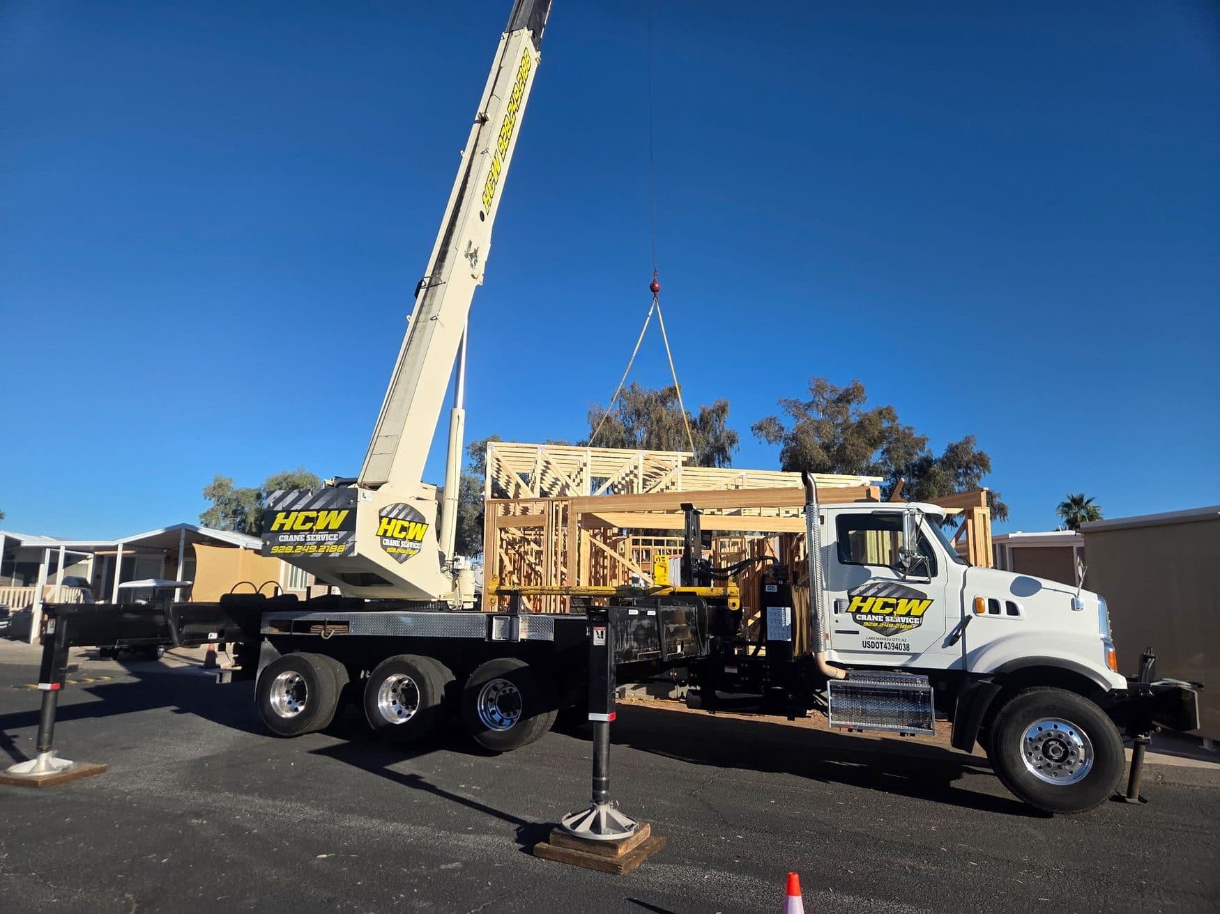 Branded boom truck crane on outriggers and wood cribbing lifting a roof truss over a new wood frame